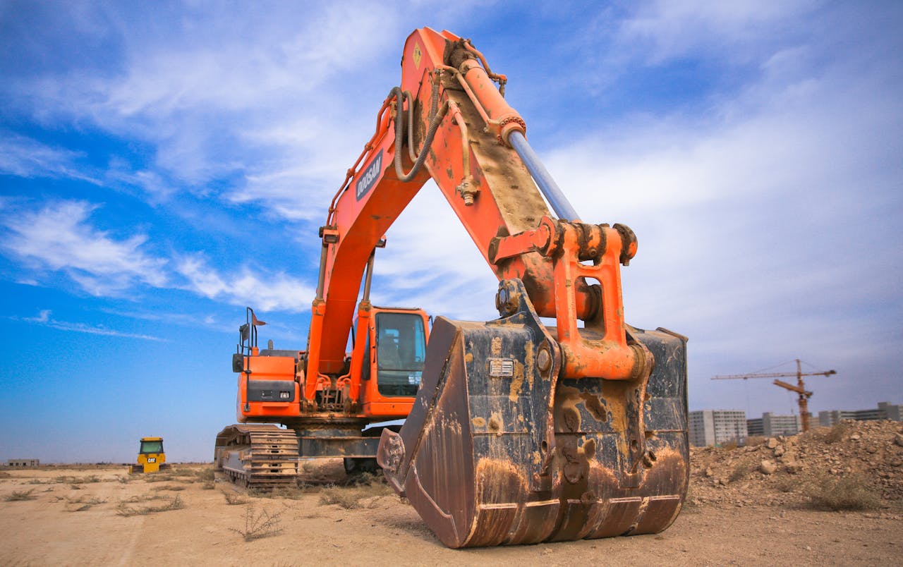 services-01 A large orange excavator working on a construction site under a blue sky.